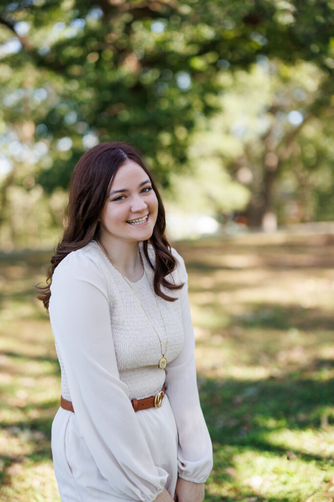 Smiling high school senior Ava in a light-colored dress and belt, posing outdoors in Hudson, Wisconsin, celebrating her graduation.