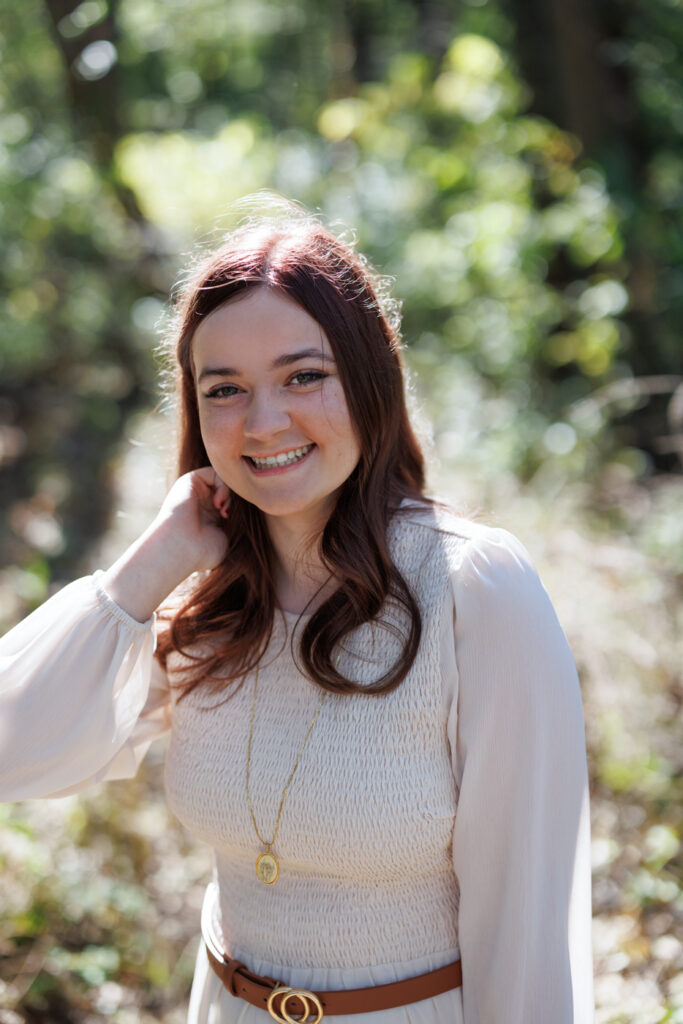 Ava smiling in a natural setting, wearing a light-colored dress and a necklace, celebrating her high school graduation in Hudson, Wisconsin.