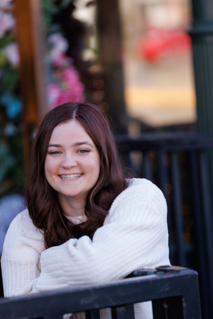Ava smiling in a cozy white sweater, posing at her high school senior session in Hudson, Wisconsin, with colorful floral background elements.