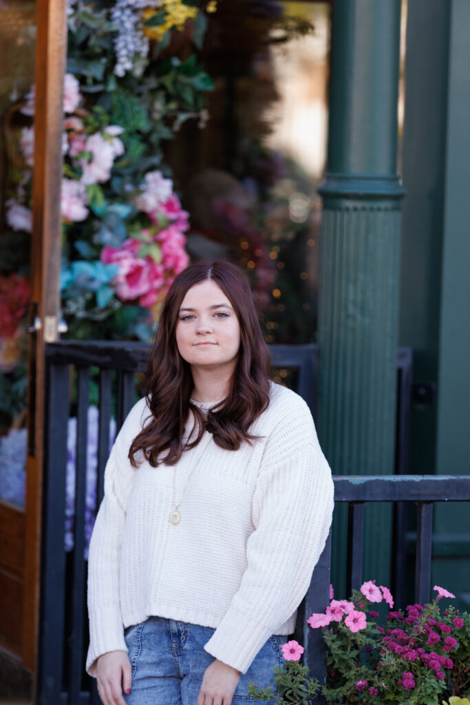 Ava posing in a white sweater against a backdrop of colorful flowers, celebrating her high school graduation in Hudson, WI.