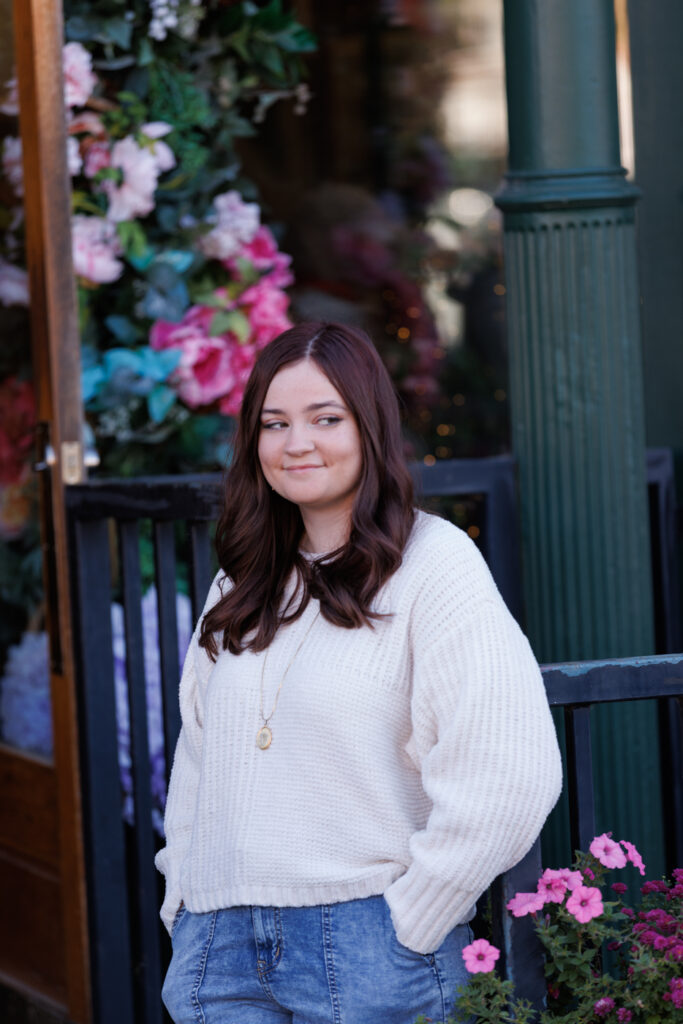 Ava smiling in a cozy sweater, standing in front of a floral backdrop during her high school senior portrait session in Hudson, Wisconsin.