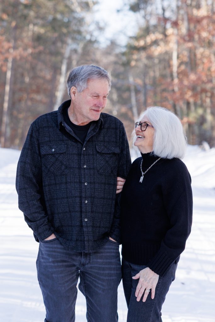 Elderly couple smiling and enjoying each other's company in a snowy winter landscape in Spooner, Wisconsin, showcasing family connection in a photography session by Superior Sunset Studio.