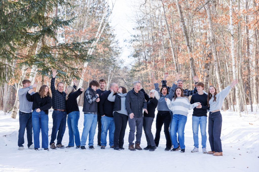 Large family gathering in a snowy forest, joyful expressions, winter clothing, Spooner, Wisconsin family photography session.