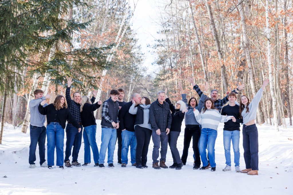 Winter family photography session in Spooner, Wisconsin, featuring a joyful group of family members posing in the snow with trees in the background.