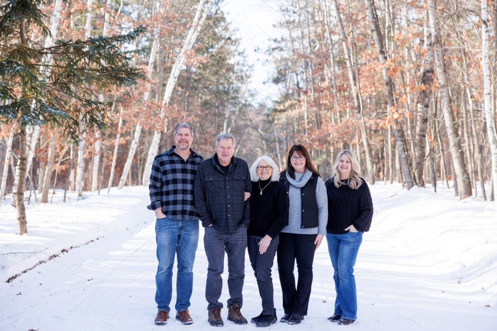 Winter family portrait in Spooner, Wisconsin, featuring five family members standing on a snowy path surrounded by trees.