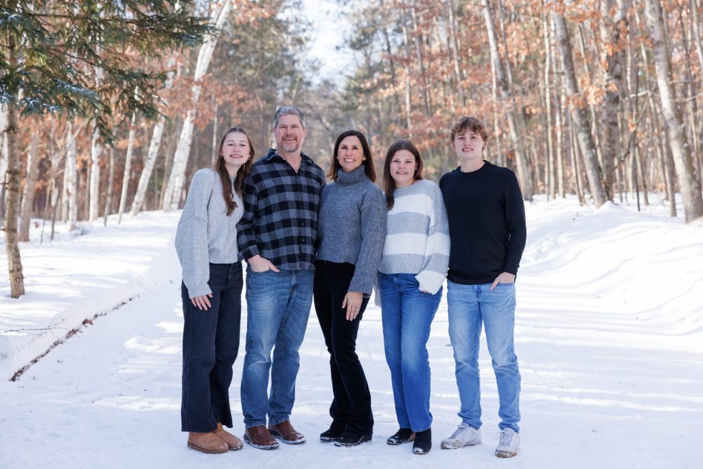 Winter family photography session in Spooner, Wisconsin, featuring a family of five posing together in a snowy forest setting.