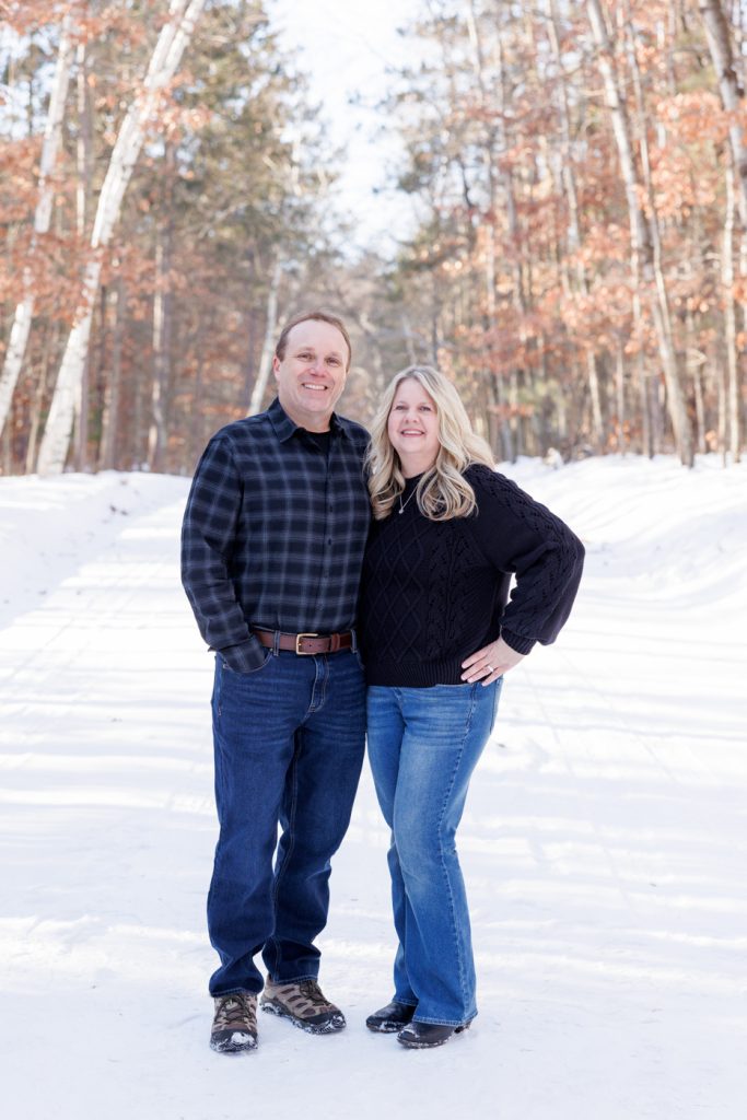 Couple posing together in a snowy forest setting, showcasing a winter family photography session in Spooner, Wisconsin.
