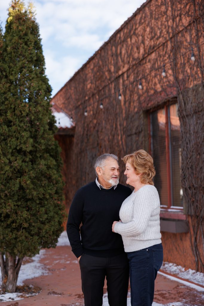 Couple Jane and Bruce smiling and embracing outdoors in Duluth, Minnesota, surrounded by winter scenery and rustic architecture, showcasing a joyful moment from their photography session.