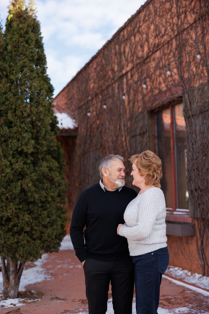Jane and Bruce sharing a joyful moment together during their winter photography session in Duluth, Minnesota, surrounded by a rustic backdrop and snow-covered ground.