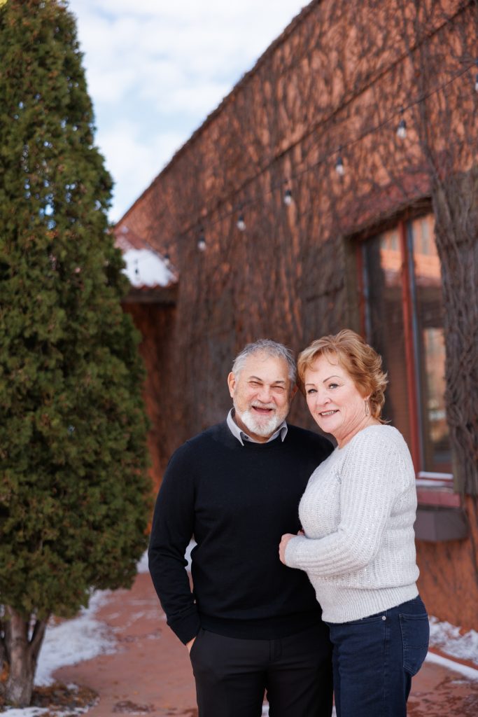 Jane and Bruce smiling together outdoors in Duluth, Minnesota, surrounded by winter scenery and rustic architecture, capturing a joyful moment from their photography session.
