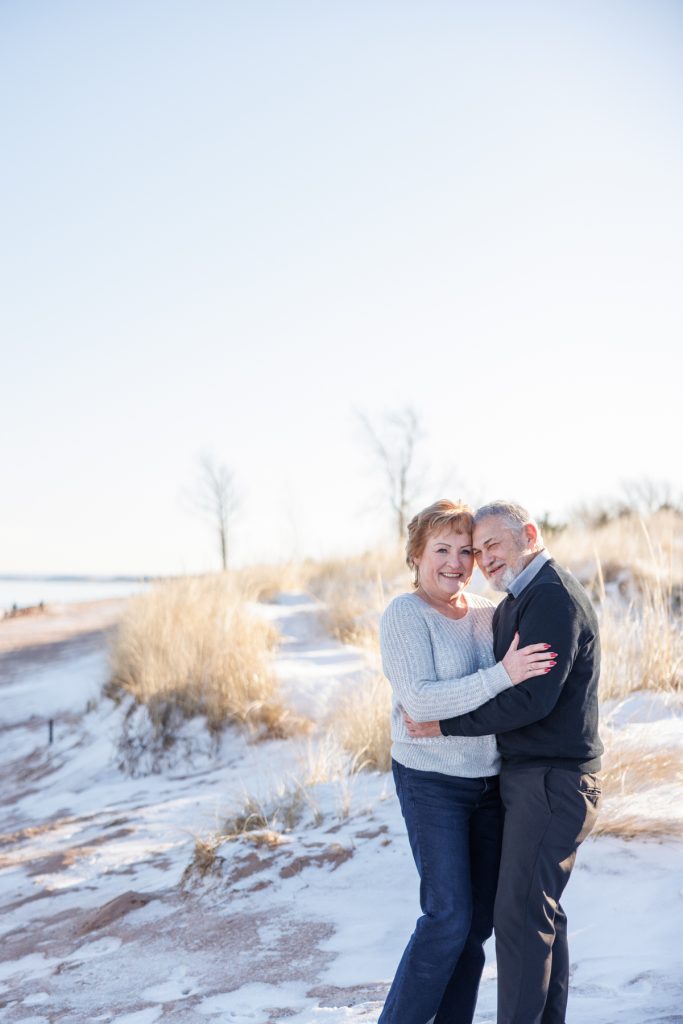 Couple embracing joyfully on a snowy beach in Duluth, Minnesota, celebrating their winter photography session by Superior Sunset Studio.