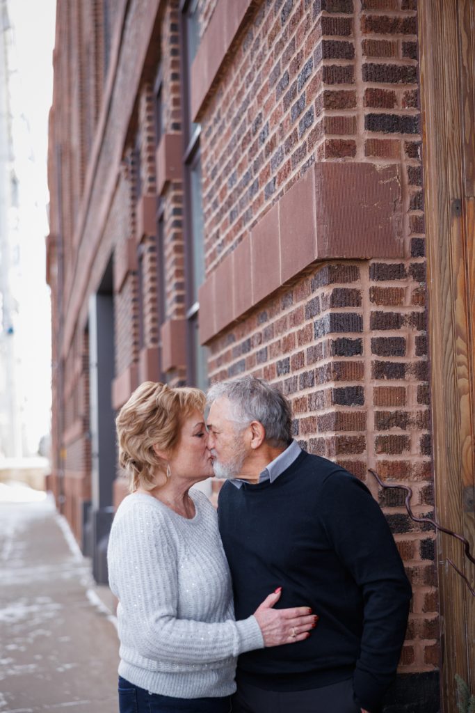 Couple Jane and Bruce sharing a kiss in a brick-lined Duluth alley during a winter photography session.