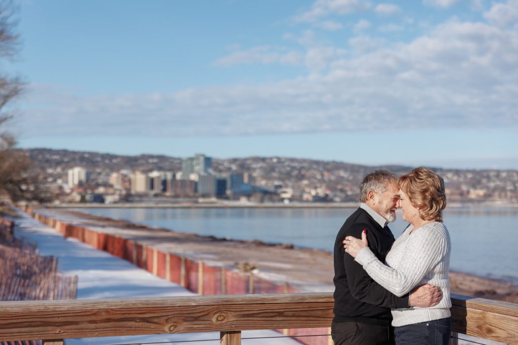Couple embracing on a wooden deck overlooking Lake Superior in Duluth, Minnesota, celebrating their winter photography session by Superior Sunset Studio.