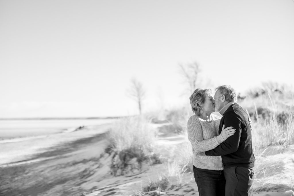 Couple Jane and Bruce sharing a kiss on a winter beach in Duluth, Minnesota, surrounded by snow and grass, celebrating their engagement during a photography session by Superior Sunset Studio.