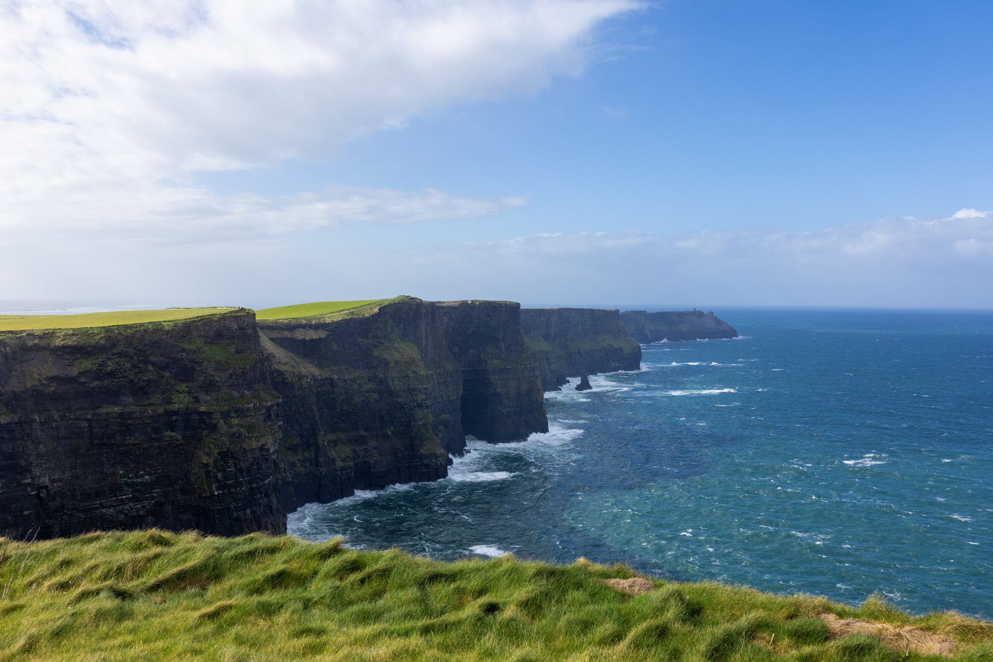 Cliffs of Moher in Ireland with lush green grass and ocean waves, representing travel photography for small group tours.
