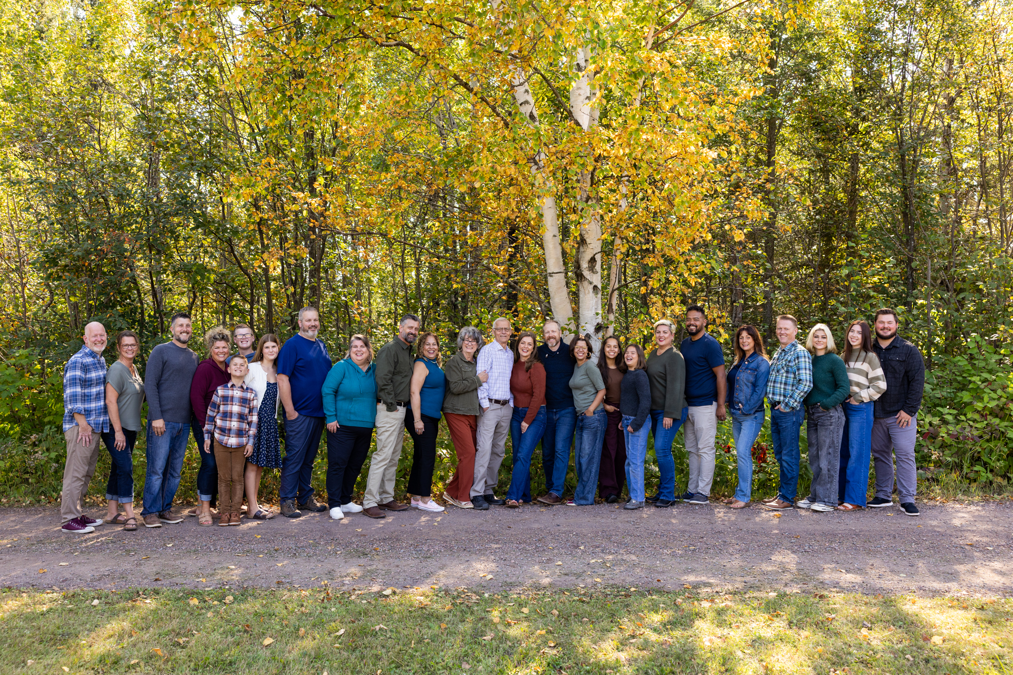 Grand Marais family session portrait featuring a diverse group of people standing together in front of autumn foliage and birch trees, showcasing family connections and seasonal colors.