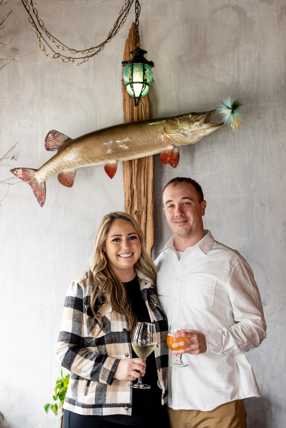 Couple holding drinks in a cozy setting with a decorative fish and lantern, representing engagement photography in a warm atmosphere.