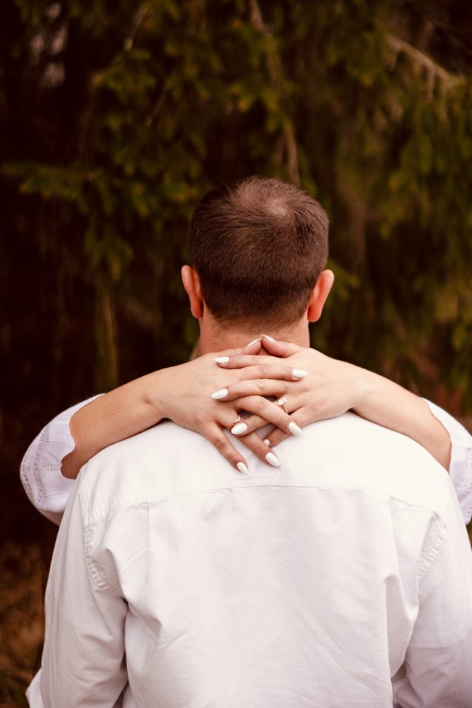 Couple embracing from behind, showcasing engagement ring and romantic connection in Hayward, WI.