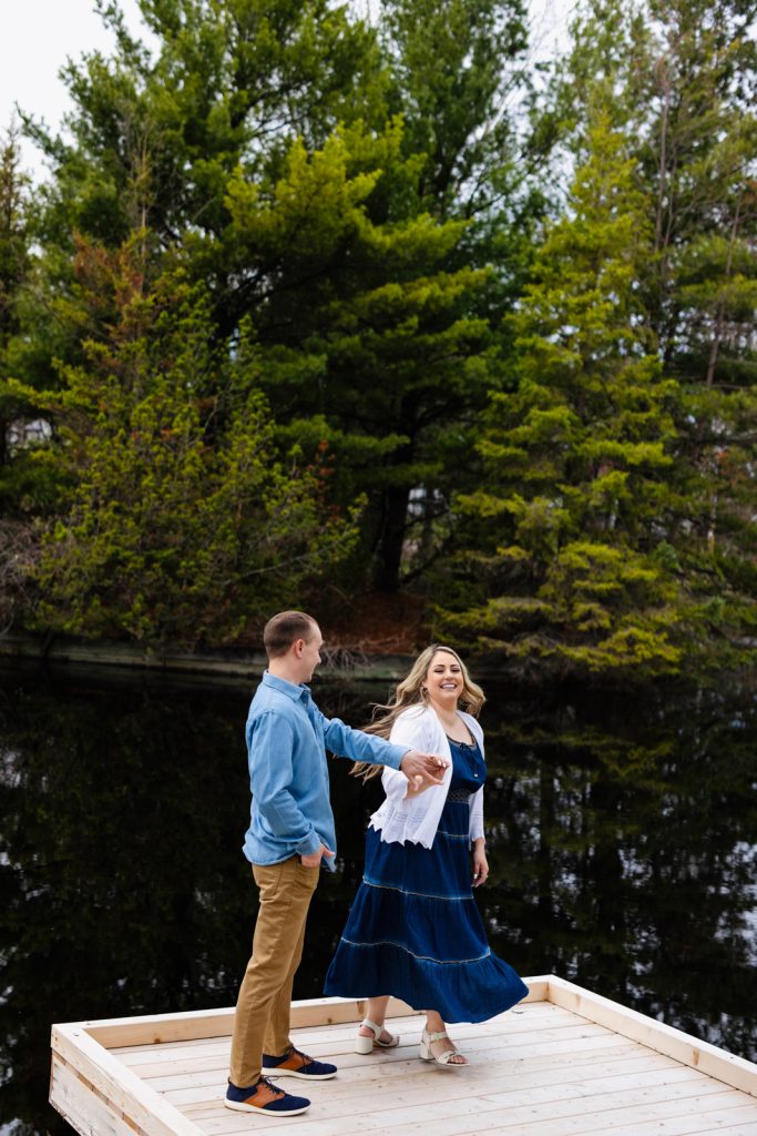 Bianca and Nick engaged on a wooden platform by water, surrounded by lush greenery, capturing a joyful moment in their Hayward, WI engagement session.