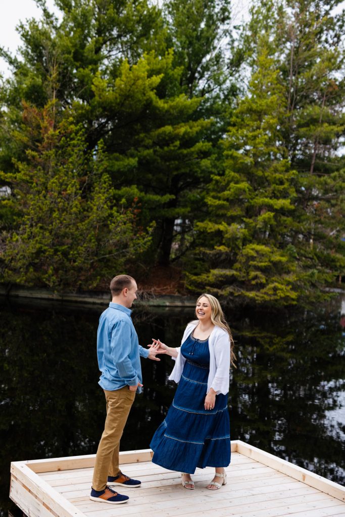 Bianca and Nick engaged on a wooden dock surrounded by lush greenery, capturing a joyful moment in Hayward, WI.