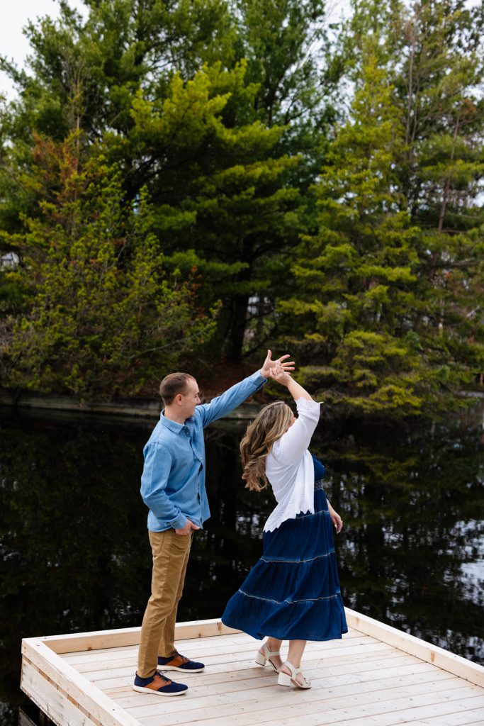 Bianca and Nick dancing on a wooden dock surrounded by greenery during their engagement session in Hayward, WI.