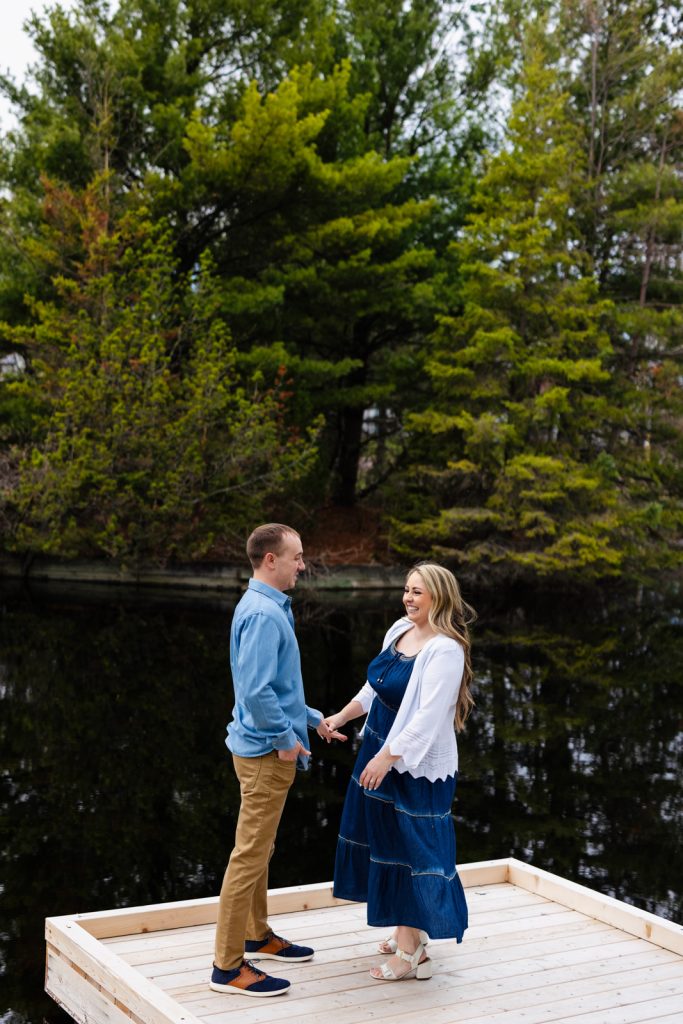 Bianca and Nick holding hands on a wooden dock surrounded by lush greenery, celebrating their engagement in Hayward, WI.