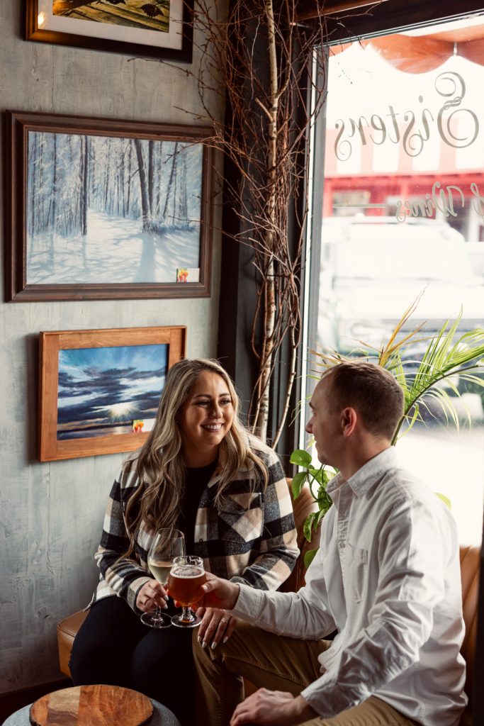 Bianca and Nick enjoying drinks in a cozy setting, surrounded by artwork, during their engagement session in Hayward, WI.