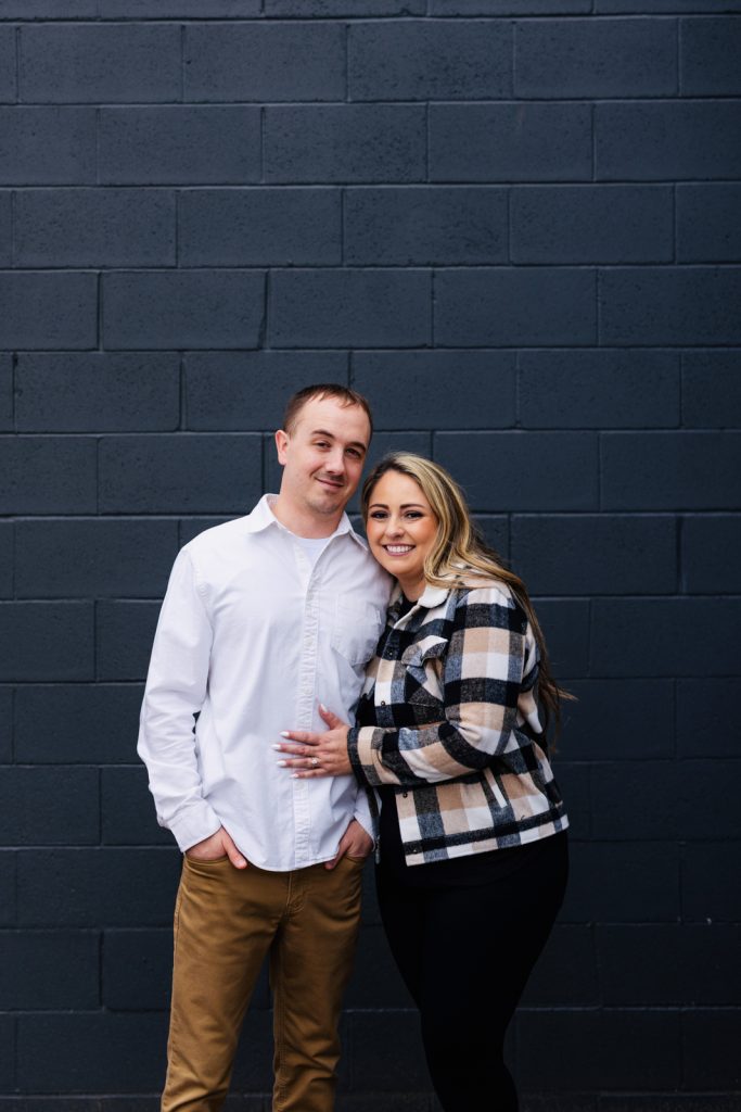 Bianca and Nick posing together in front of a gray wall during their engagement session in Hayward, WI, showcasing their love and excitement for their upcoming wedding.