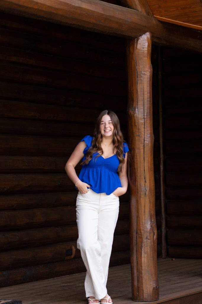 Julia's senior portrait in Hayward, WI, leaning against a rustic log cabin.