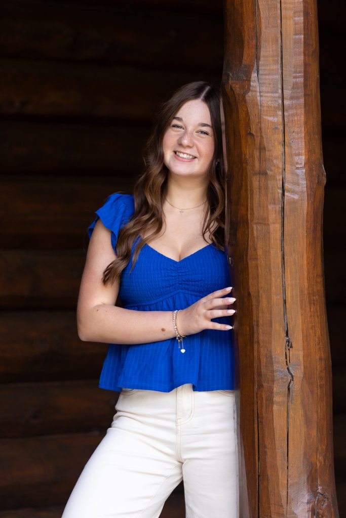 Julia's senior portrait session in Hayward, WI, showcasing a smiling graduate leaning against a rustic