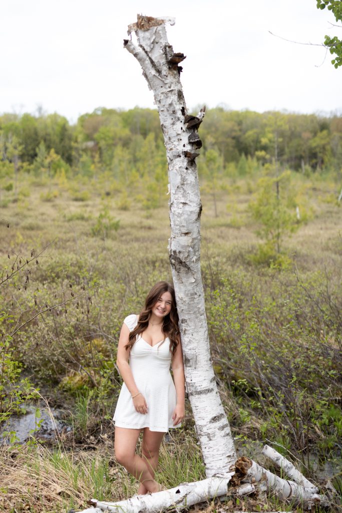 Julia's senior portrait in Hayward, WI, leaning against a birch tree in a natural setting.