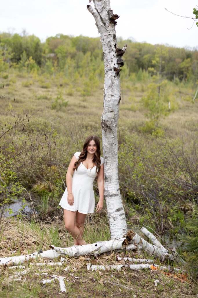 Julia's senior portrait in Hayward, WI, leaning against birch tree in natural setting.
