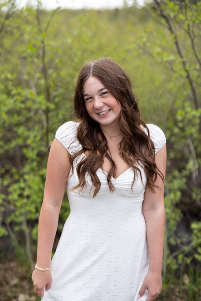Julia's senior portrait in Hayward, Wisconsin, smiling in a white dress among spring foliage.