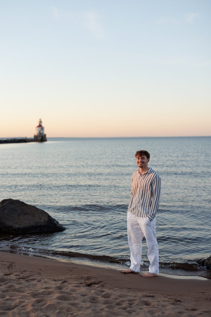 Senior portrait of Jaymeson on Duluth beach with Superior, Wisconsin lighthouse in background.