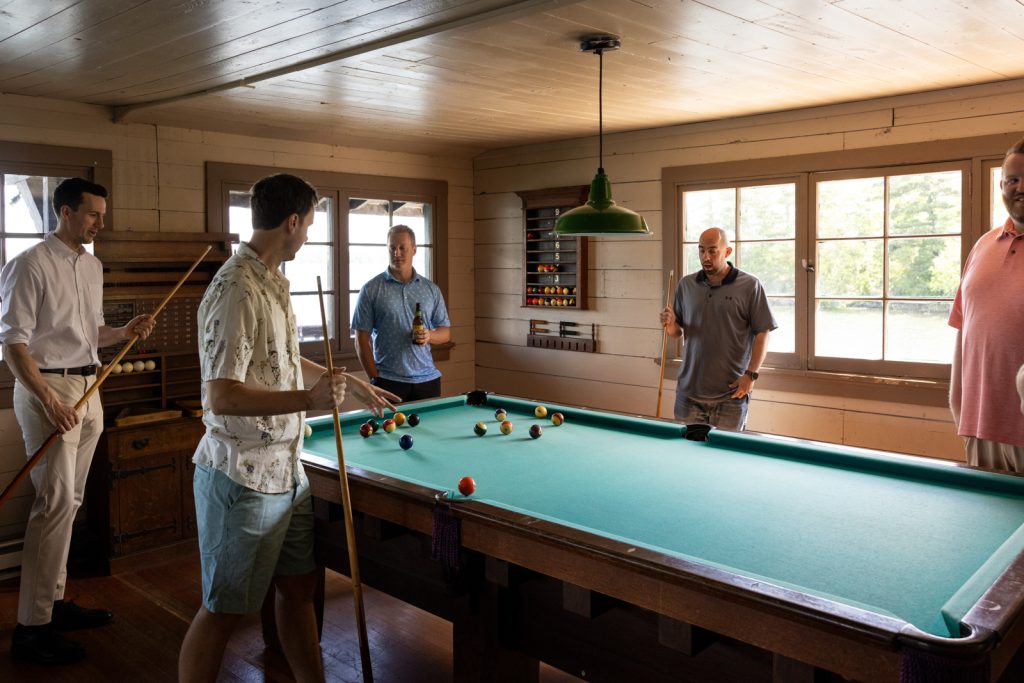 Brittany and Cole's Stout’s Island wedding party playing pool in the boat house lodge.