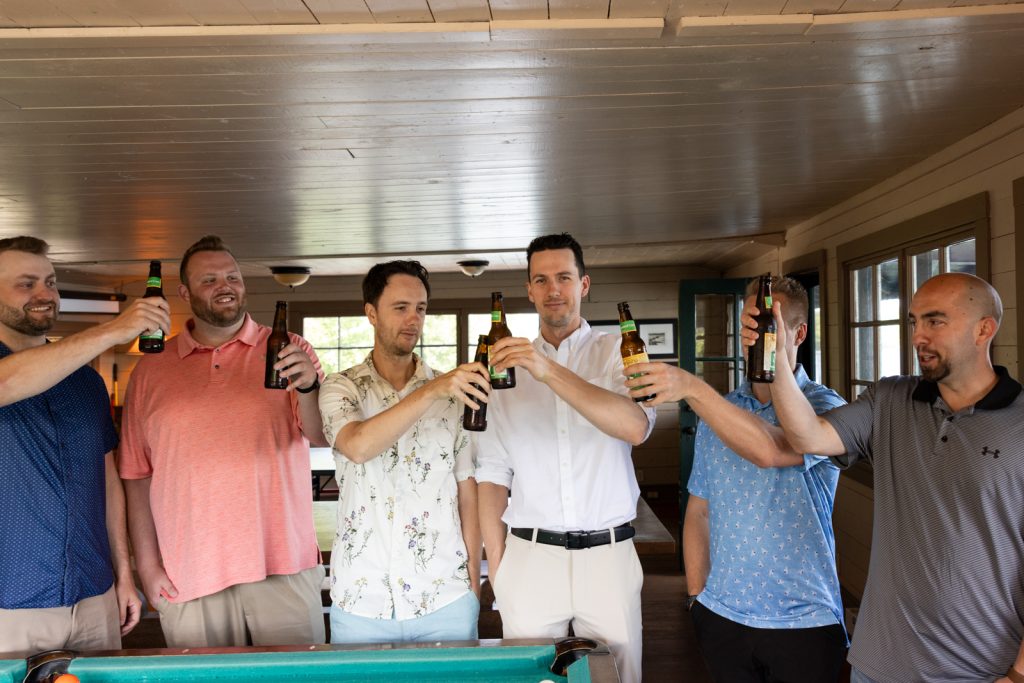 Brittany and Cole’s Stout’s Island wedding party toasting with beer under the boat house roof.