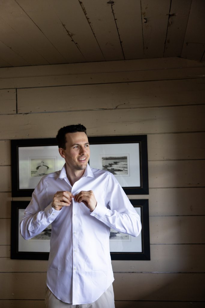 Brittany and Cole’s Stout’s Island wedding: groom getting ready in white shirt and tan pants.