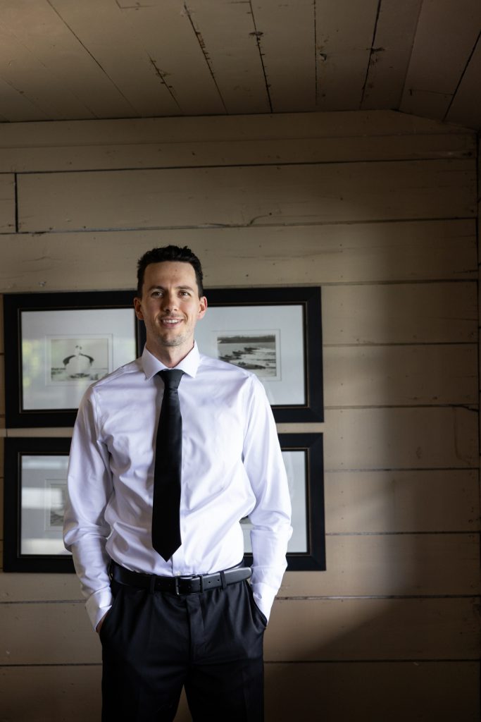 Brittany and Cole's wedding groom in suit and tie, posed in Stout’s Island boat house,