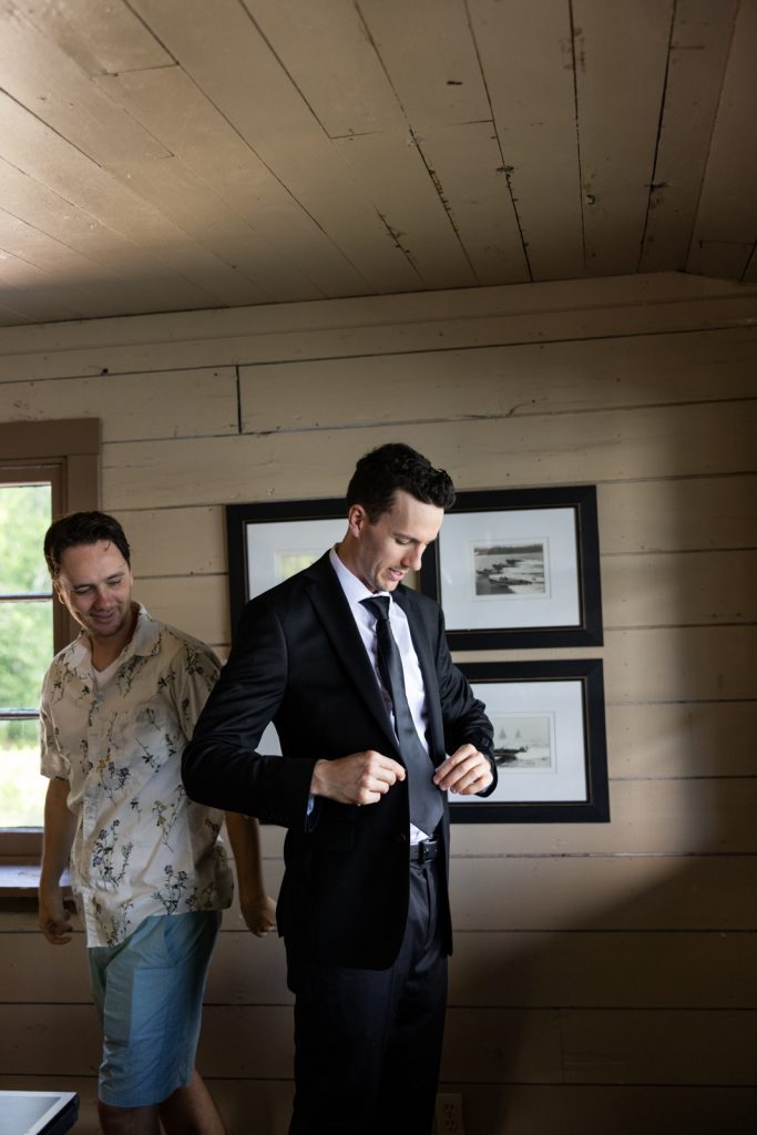 Brittany and Cole's Stout’s Island wedding: Groom adjusting tie in a boat house setting.