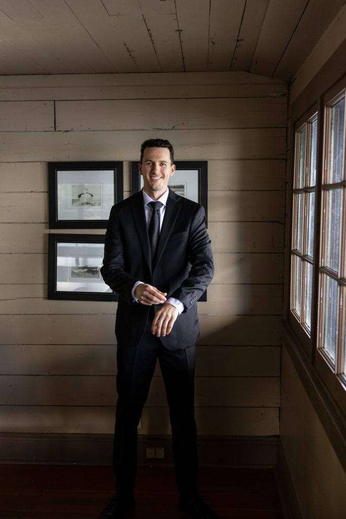 Groom in suit posing near framed photos at Stout’s Island Lodge wedding venue.