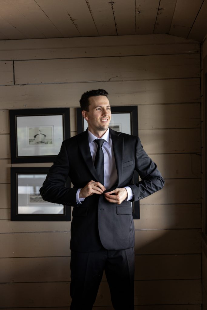 Brittany and Cole’s wedding groom in a suit adjusting his jacket at Stout’s Island Lodge,
