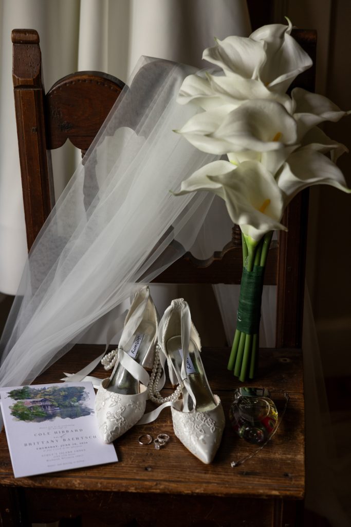 Bride's veil, bouquet of calla lilies, and wedding shoes on a vintage wooden table at