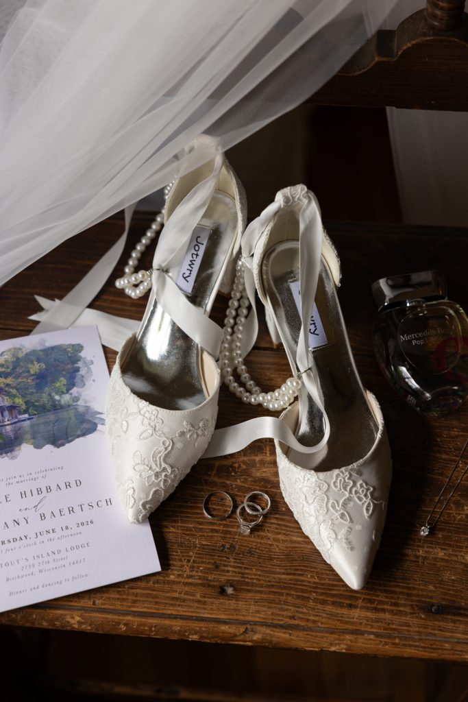 Bride's wedding shoes and pearl necklace with wedding rings and invitation on a wooden surface