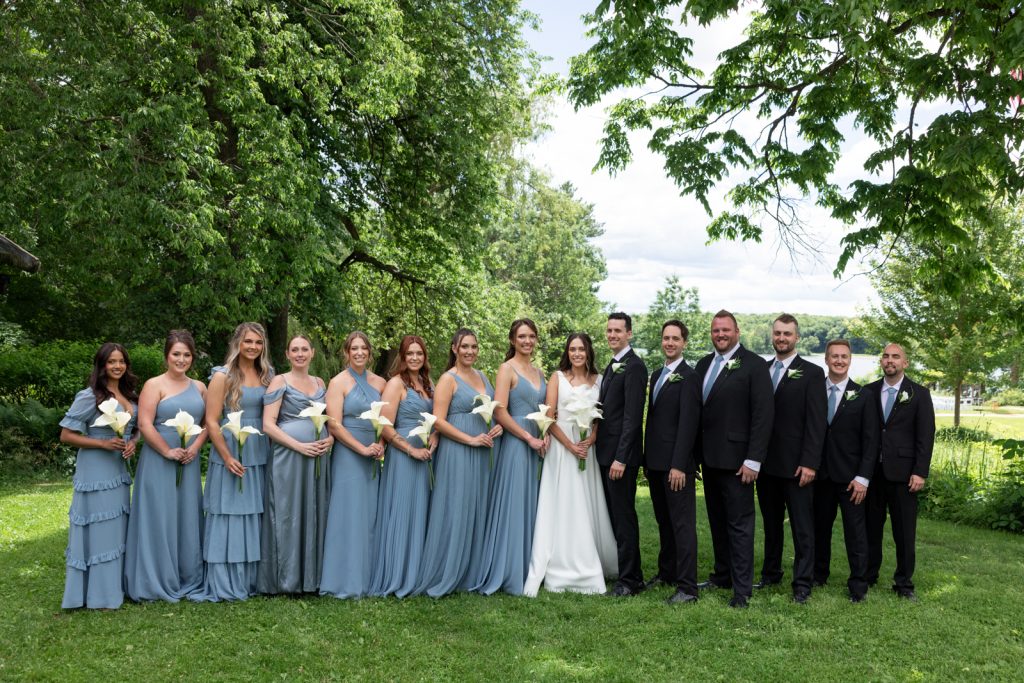 Brittany and Cole's Stout’s Island wedding party in blue dresses and black suits, lakeside setting.