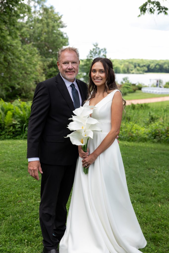 Brittany and Cole, the wedding couple, posing with a large white floral bouquet on Stout’s