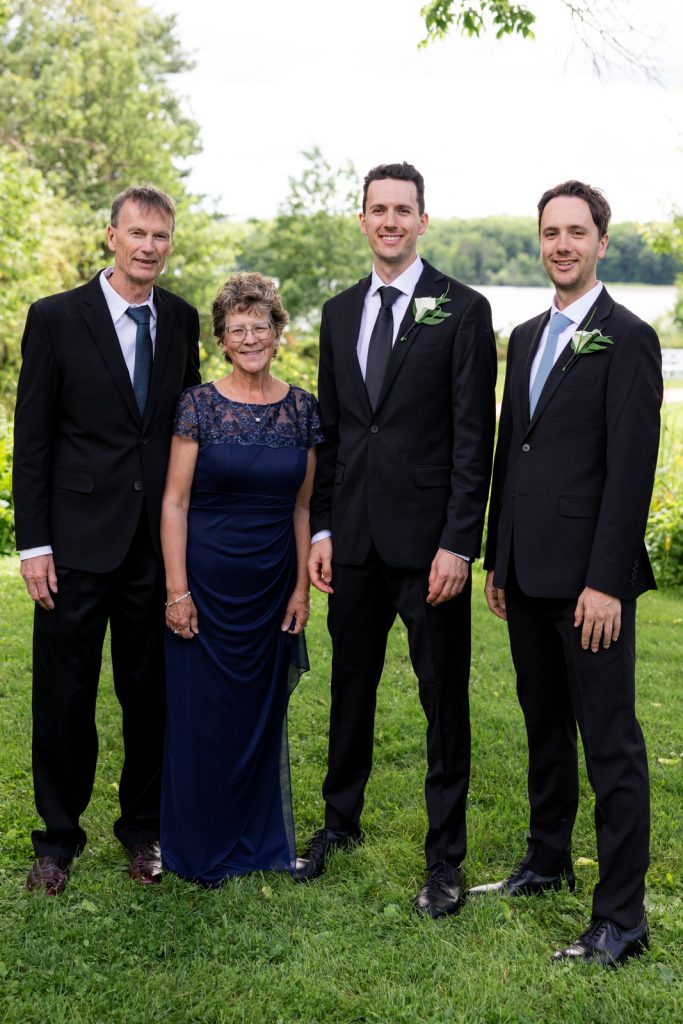 Brittany and Cole's Stout’s Island wedding: Groom with parents and groomsmen by Red Cedar Lake.