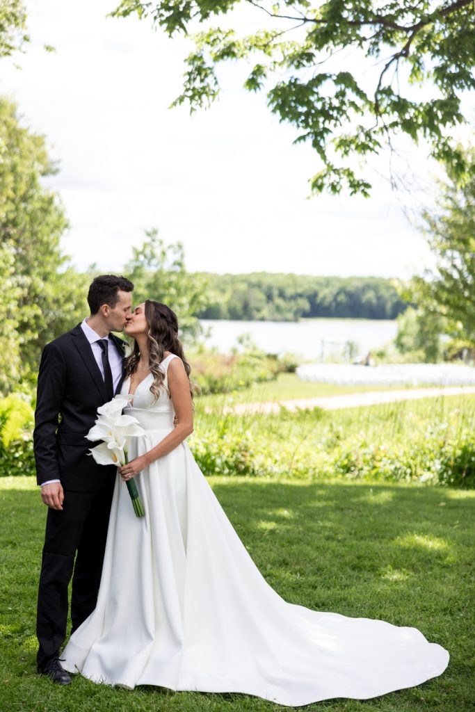 Brittany and Cole kissing on Stout’s Island wedding day, Red Cedar Lake in the background.