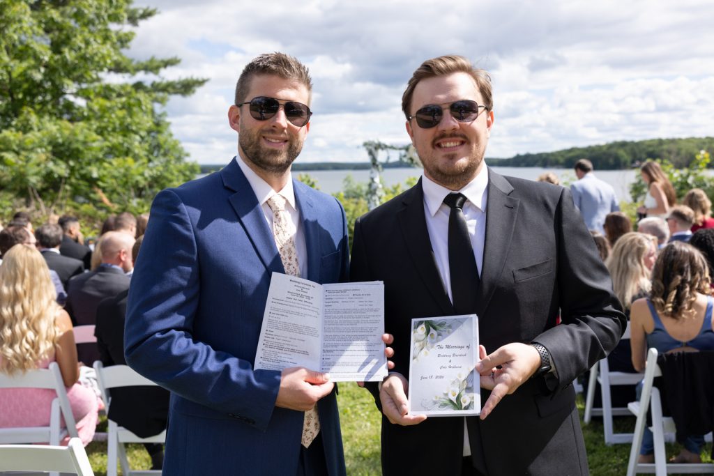Groomsmen holding wedding programs at Stout’s Island wedding ceremony on Red Cedar Lake.