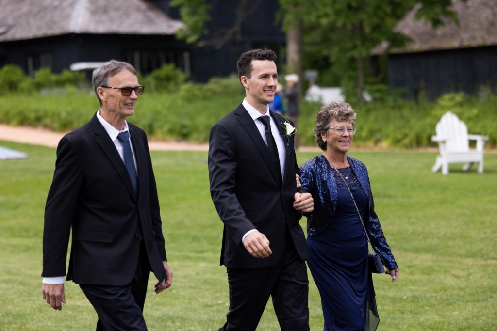 Brittany and Cole’s Stout’s Island wedding: Groom and parents walking on the lawn of the