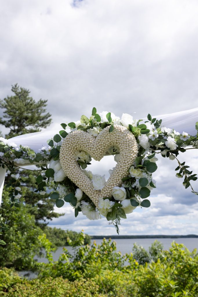 Floral heart decoration on wedding arch overlooking Red Cedar Lake at Stout’s Island wedding.